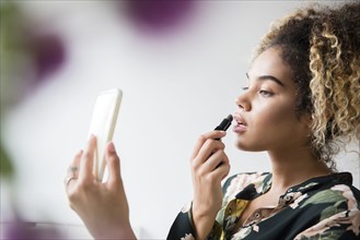 Mixed Race woman holding cell phone applying lipstick