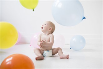 Caucasian baby boy sitting on floor watching balloons