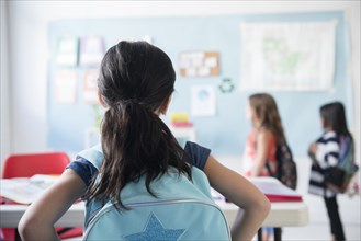 Girl in classroom wearing backpack watching classmates
