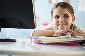 Smiling Caucasian girl leaning on notebooks at desk