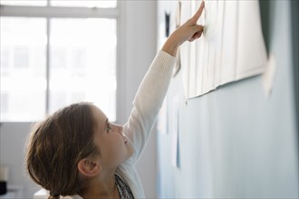 Caucasian girl pointing to paper on wall
