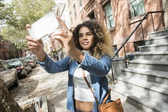Mixed Race woman in city posing for cell phone selfie