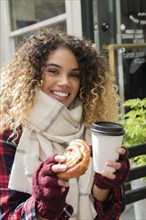 Smiling Mixed Race woman showing donut and coffee cup