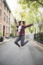 Mixed Race woman jumping for joy in city