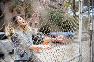 Laughing Mixed Race woman holding chain-link fence in city