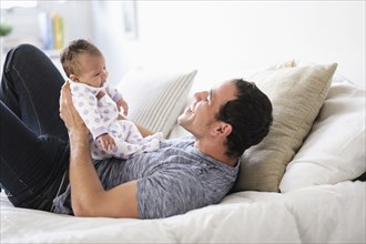 Hispanic father playing with baby daughter on bed