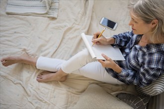 Caucasian woman sitting on bed writing on cell phone