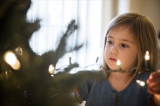 Caucasian girl hanging lights on Christmas tree