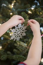Caucasian girl hanging snowflake ornament on Christmas tree