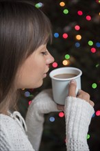 Mixed Race woman drinking coffee near Christmas tree