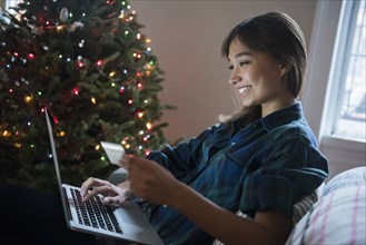Mixed Race woman online shopping with laptop near Christmas tree
