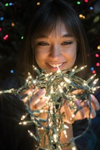 Mixed Race woman holding string lights near Christmas tree