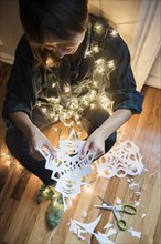 Mixed Race woman sitting on floor wrapped in string lights holding snowflake