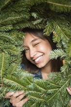 Mixed Race woman winking in pine wreath
