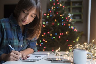 Mixed Race woman writing on card near Christmas tree