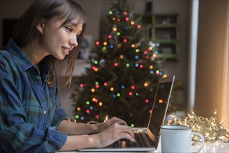 Mixed Race woman using laptop near Christmas tree
