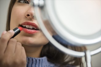 Mixed Race woman applying lipstick in mirror