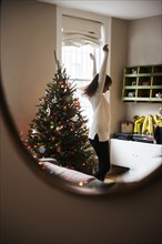 Reflection of Mixed Race woman dancing near Christmas tree