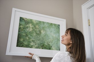 Mixed Race woman hanging picture frame on wall