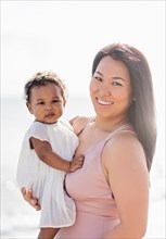 Portrait of mother holding baby daughter near ocean