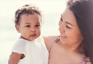 Portrait of mother holding baby daughter near ocean