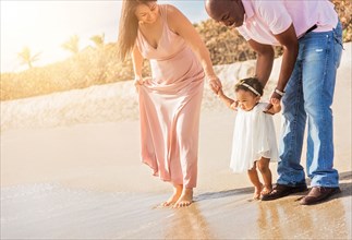 Couple holding hands of baby daughter walking on beach