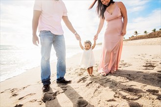 Couple holding hands of baby daughter walking on beach