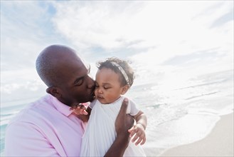 Father kissing cheek of baby daughter on beach