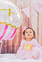 Mixed Race baby girl sitting near birthday balloon