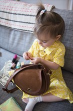 Caucasian baby girl playing with purse on sofa