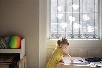 Caucasian baby girl coloring on sketchpad near window