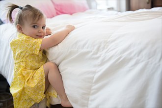 Caucasian baby girl climbing on bed