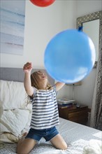 Caucasian girl kneeling on bed playing with balloons