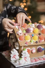 Hands of Caucasian girl decorating gingerbread house with candy
