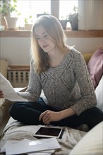Woman sitting on sofa paying bills with digital tablet