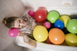 Smiling woman sitting in bathtub with multicolor balloons