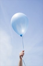Hand of Caucasian girl holding blue balloon in blue sky