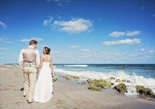 Caucasian bride and groom walking on beach