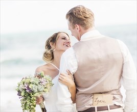 Caucasian bride and groom hugging on beach