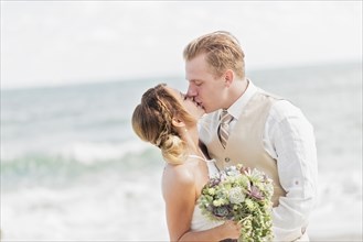 Caucasian bride and groom kissing on beach