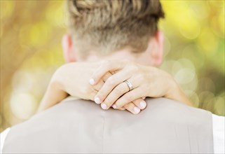 Hands of Caucasian bride hugging groom outdoors