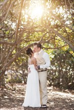 Caucasian bride and groom kissing under trees