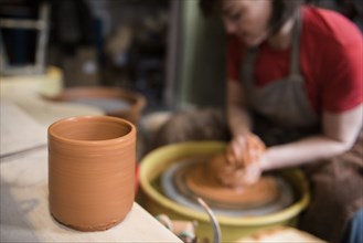 Cup near Caucasian woman shaping pottery clay on wheel