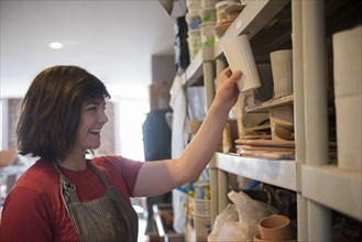 Smiling Caucasian woman placing cup on shelf in workshop