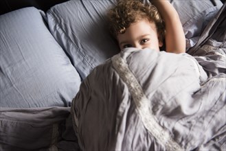 Caucasian boy hiding under blanket in bed
