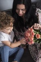 Caucasian mother sitting on sofa with son examining flowers