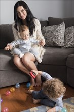 Caucasian mother sitting on sofa playing with sons