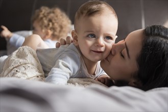 Caucasian mother laying on bed kissing baby son