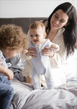 Caucasian mother kneeling on bed playing with sons