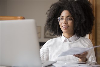 African American woman holding paperwork using laptop